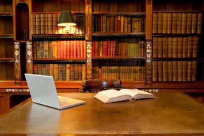 A laptop and open book sitting on table in a library.