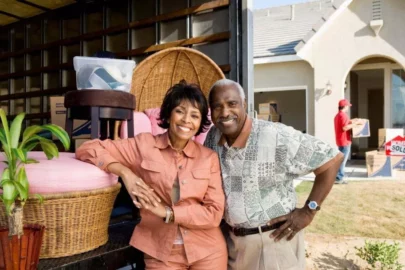 man and woman standing next to a moving truck full of furniture at their new home