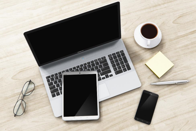 A computer, phone, and tablet sit on a table.