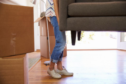 A woman carries one end of a couch