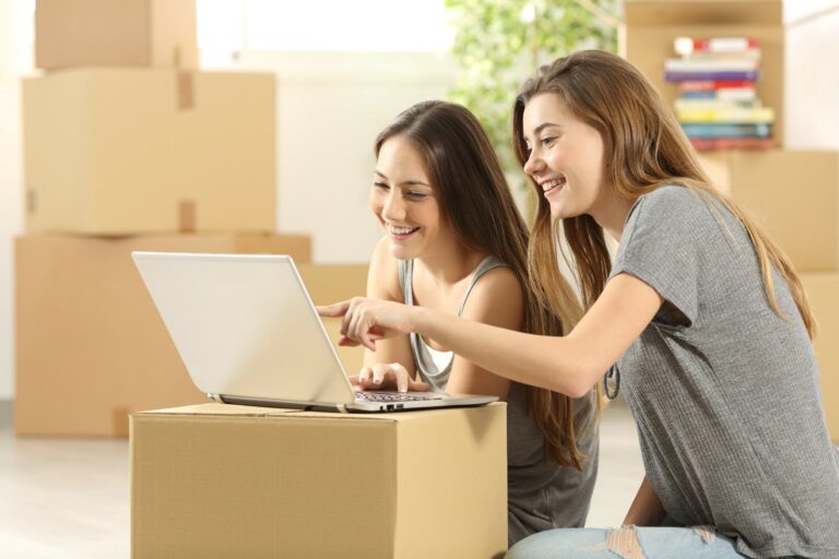 Two girls sitting on the floor looking at a computer and pointing to the screen.