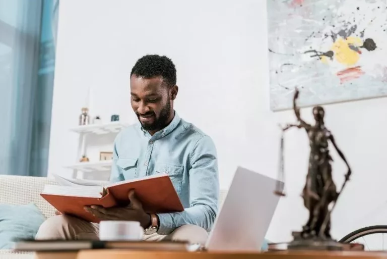 Man reading book on a couch inside an apartment.