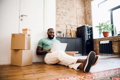 Man using laptop while sitting on floor next to storage boxes.