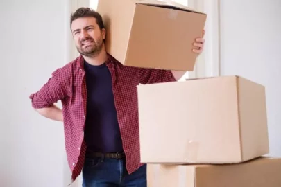 Man grabbing his hurt back while moving storage boxes.