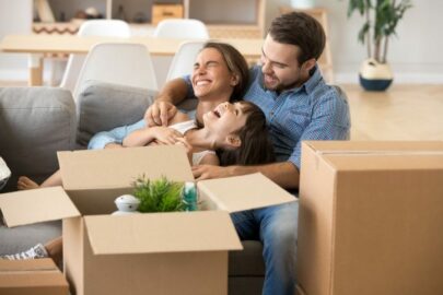 A smiling family sitting on their couch among moving boxes.