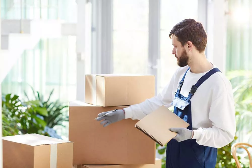 young male mover in uniform making notes while working at place of delivery