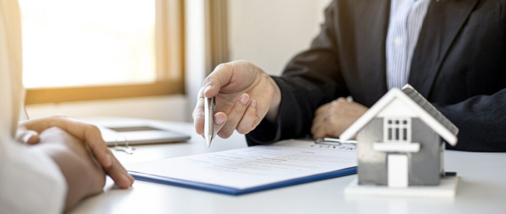 a person is pointing with a pen to a clipboard of mortgage documents