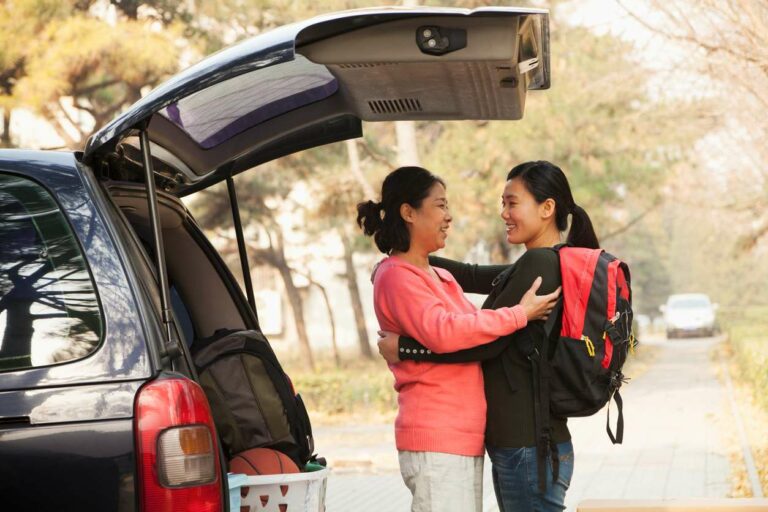 Mother and daughter embrace behind car loaded with items packed for college