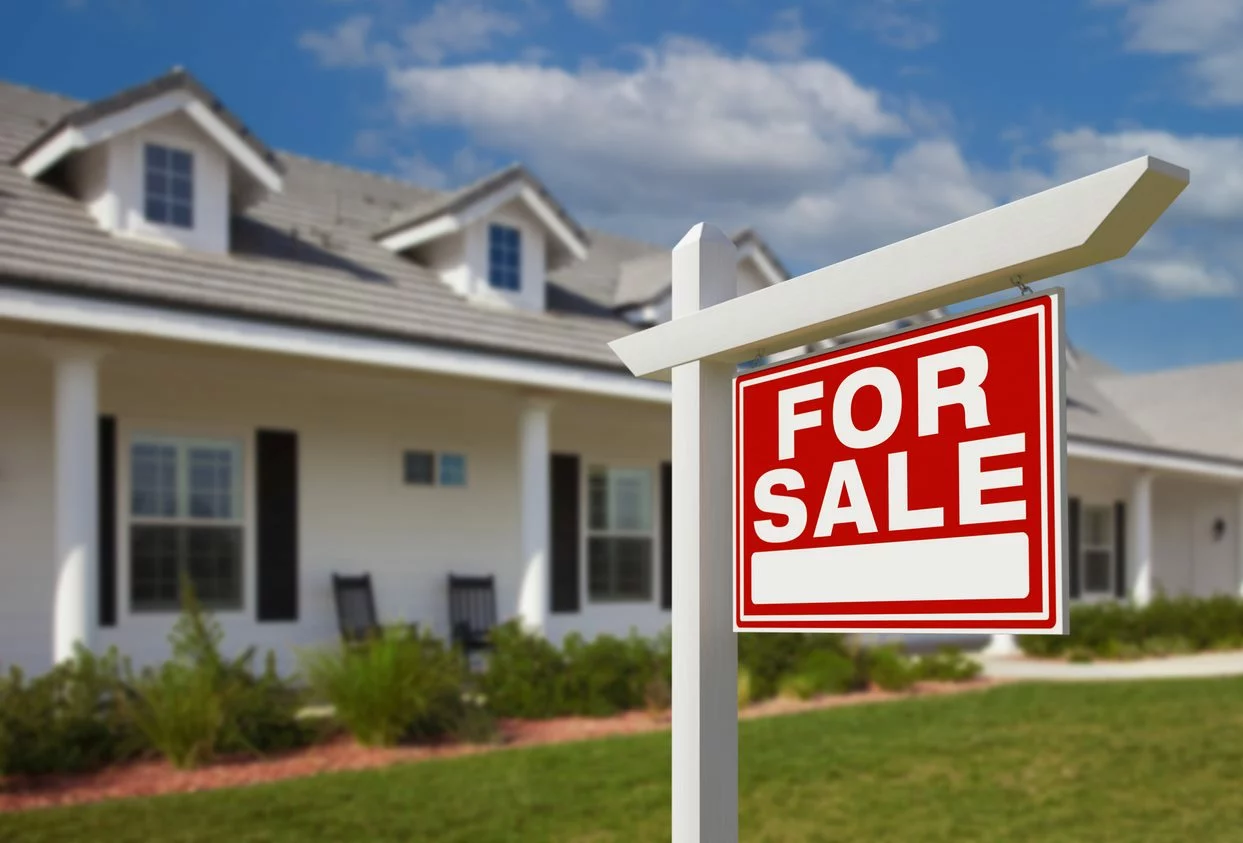 A red sign reads “For Sale” on the lawn of a home.