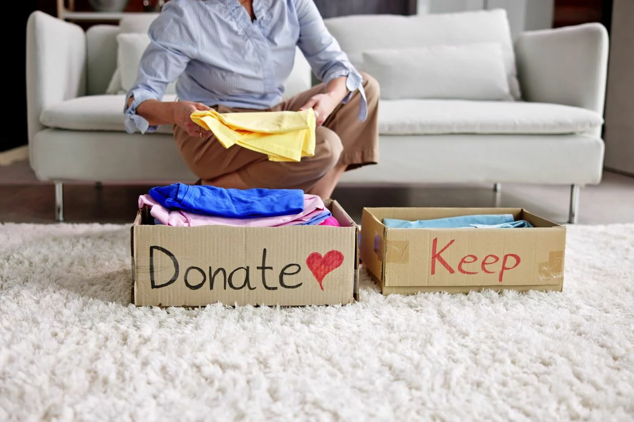 A person sitting on the couch sorts between clothes to donate and keep.