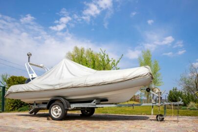 A modern inflatable motor boat with a cover sits on a steel trailer and is ready for storage.