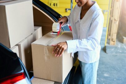 A young woman tapes a cardboard box in the back of her car.