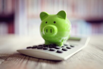 A small green ceramic piggy bank sits on top of a calculator.