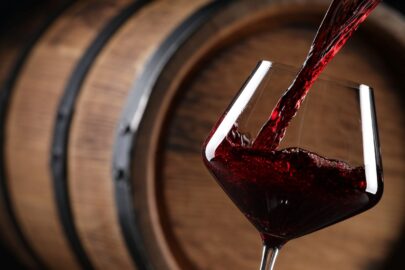 Red wine poured into a glass in front of a wooden barrel.