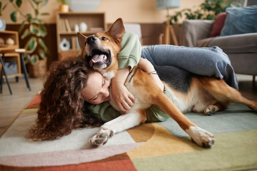 A woman plays with her dog on a rug in her apartment.